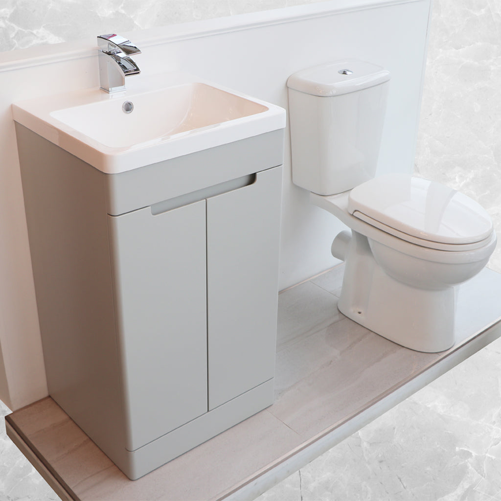 Modern white toilet and grey bathroom vanity unit with basin on tiled floor