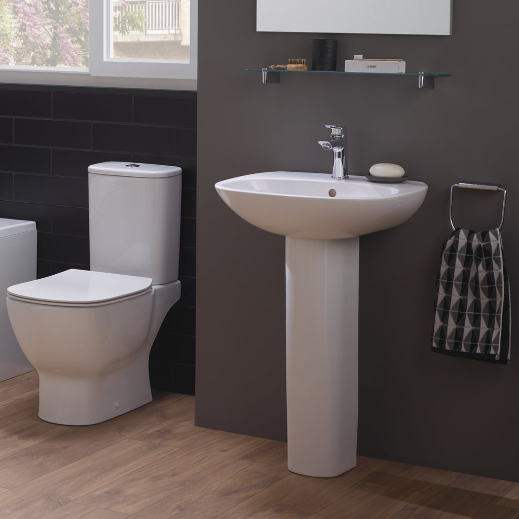 Modern bathroom with white pedestal sink, toilet, towel ring, and wooden flooring