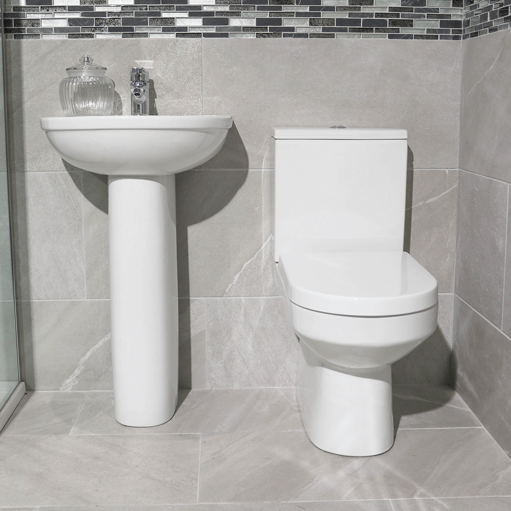 Modern bathroom with white pedestal sink, toilet, grey tiles, and mosaic tile accent wall.