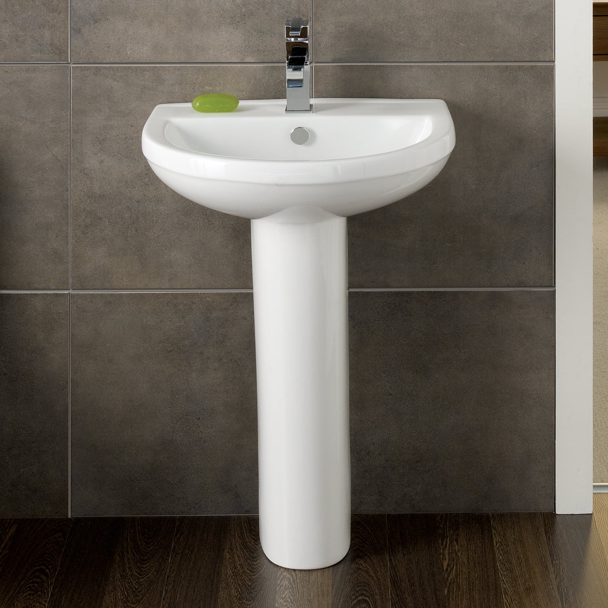 Modern white pedestal bathroom sink with chrome tap and soap, set against tiled wall