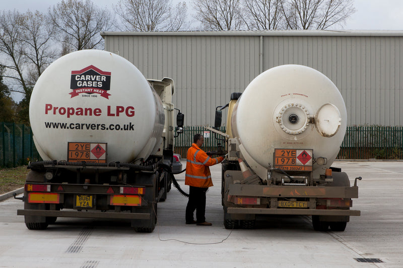 Two propane LPG delivery trucks and worker in hi-vis jacket at supply yard