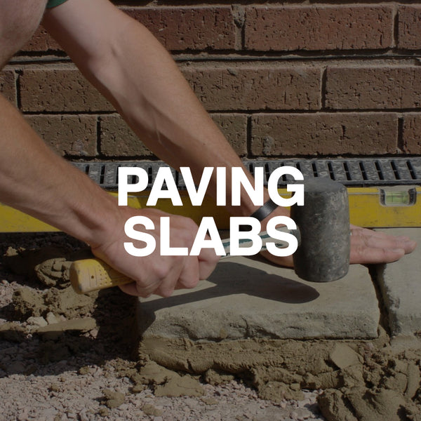 Laying paving slabs with a rubber mallet against a brick wall, level tool visible