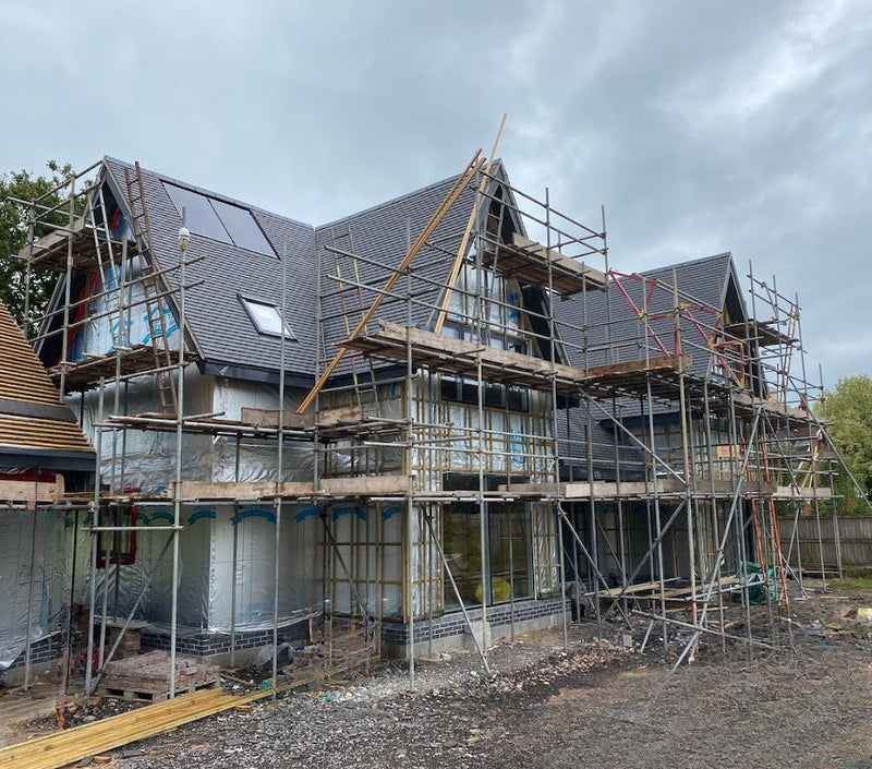 Modern house under construction with scaffolding, pitched slate roof, and insulated walls